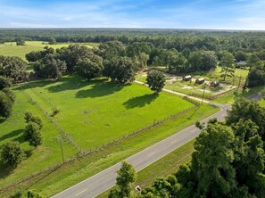A rural landscape with a fenced field, a road, and a few buildings.