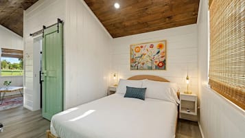 Un dormitorio con cama, mesitas de noche, una puerta verde, un cuadro y una ventana con persianas.