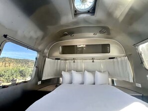 Un dormitorio con cama, cabecera y ventana con vistas a un bosque.