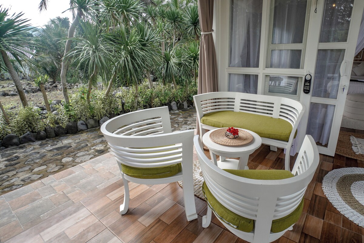 A patio with white chairs and a table, a bed with a white canopy, and a view of tropical plants.