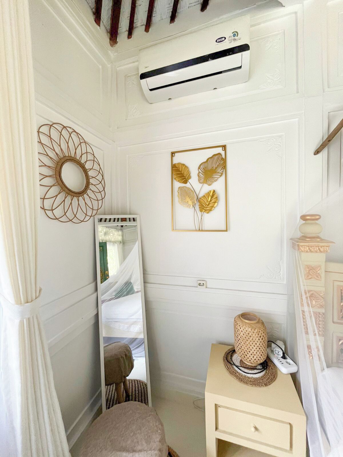 A bedroom with a bed, a bedside table, a mirror, an air conditioning unit, and decorative wall art.