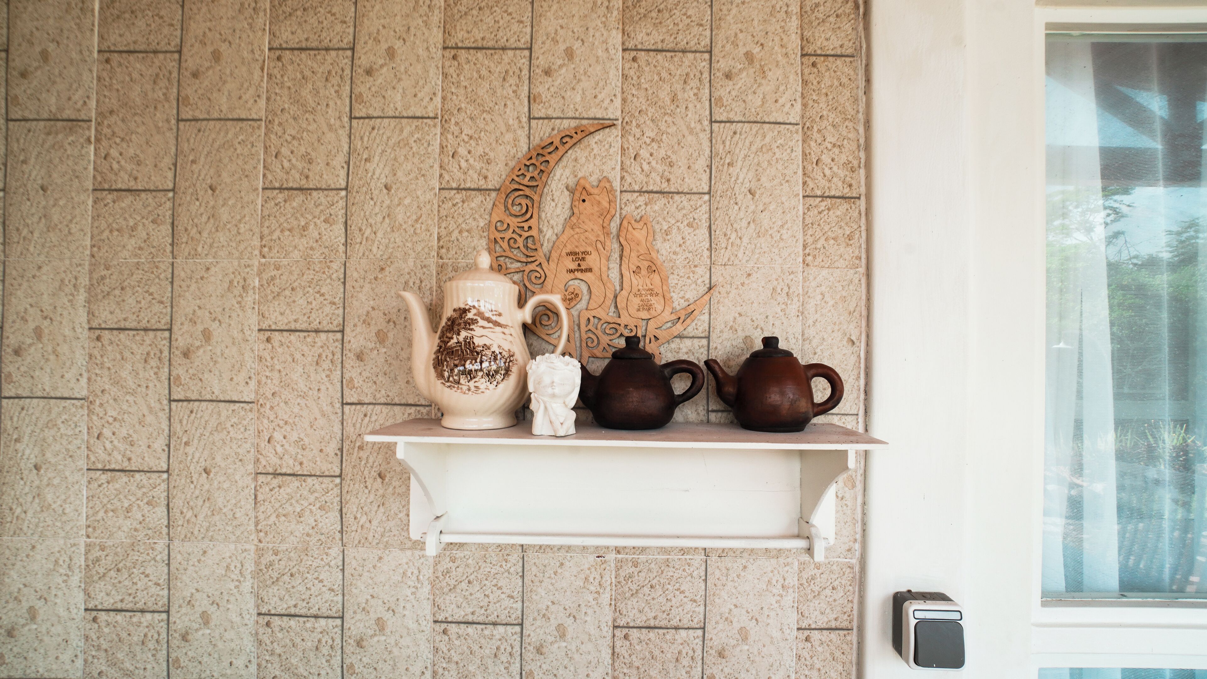 Una repisa con teteras de cerámica y un adorno frente a una pared con azulejos.
