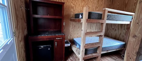 A compact room with a bunk bed, a small wooden cabinet, and a window.