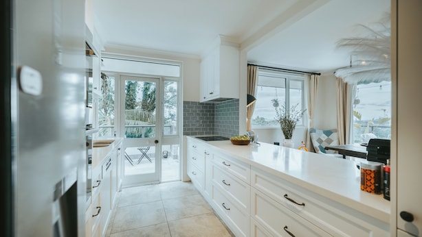Una cocina moderna con armarios blancos, salpicadero de azulejos y un amplio ventanal que proporciona luz natural.