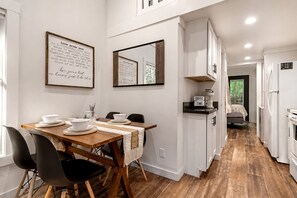 A modern kitchen with white cabinetry, a wooden dining table set with plates and bowls, and a coffee maker on the counter. - Luxurious Tiny Cabin with Hot-Tub and Fire Pit in Tennessee (Monteagle)