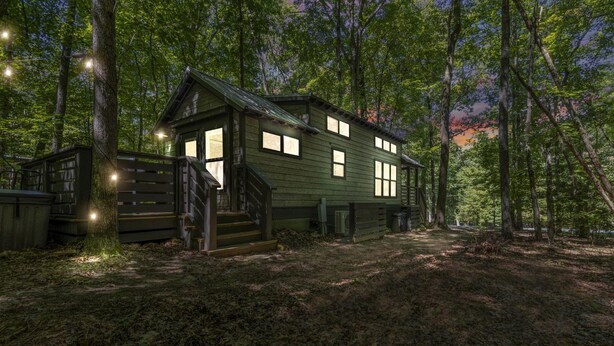 A rustic cabin with a porch, a staircase, and a forested backdrop. - Luxurious Tiny Cabin with Hot-Tub and Fire Pit in Tennessee (Monteagle)