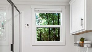 A bathroom with a toilet, a window with a view of trees, a towel rack, and a shower area. - Luxurious Tiny Cabin with Hot-Tub and Fire Pit in Tennessee (Monteagle)