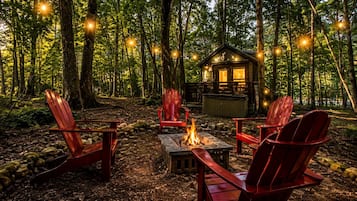 A forest cabin with a fire pit and red Adirondack chairs.