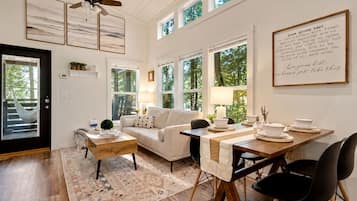 A well-lit living room with a sofa, coffee table, and dining area with chairs and a table set for a meal.