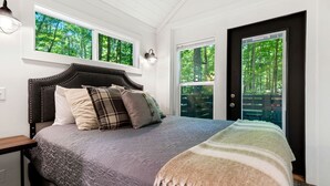 A bedroom with a bed, a nightstand, a window, and a door. - Luxurious Tiny Cabin with Hot-Tub and Fire Pit in Tennessee (Monteagle)