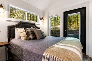 A bedroom with a bed, a nightstand, a window, and a door. - Luxurious Tiny Cabin with Hot-Tub and Fire Pit in Tennessee (Monteagle)