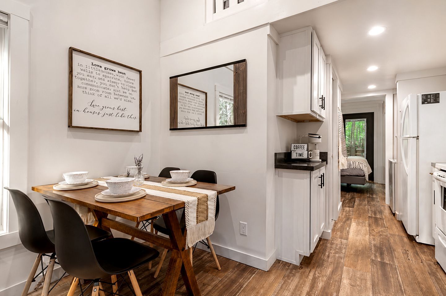 A modern kitchen with white cabinetry, a wooden dining table set with plates and bowls, and a coffee maker on the counter.