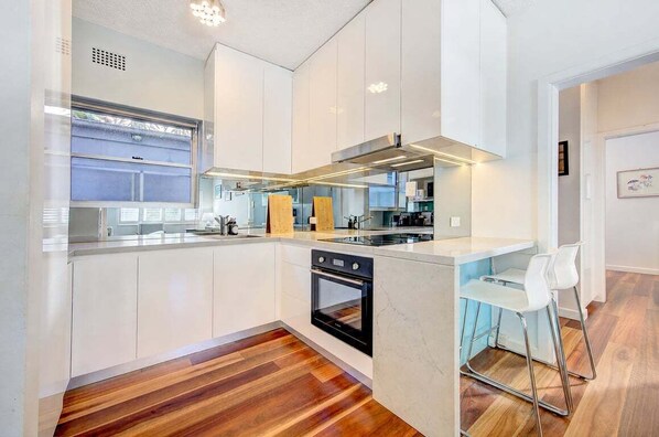 A modern kitchen with white cabinetry, a built-in oven, and a bar area with stools.