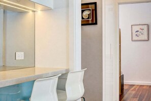 Een moderne badkamer met een grote spiegel, witte stoelen en een houten vloer.