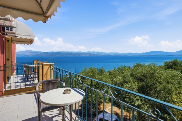 A balcony with a table and chairs, overlooking a body of water and distant mountains.
