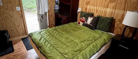 Una habitación con paneles de madera, una cama, una mesita de noche, una lámpara y un ventanal.