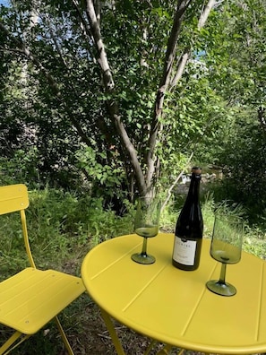 A yellow outdoor table with a bottle of wine and two glasses.