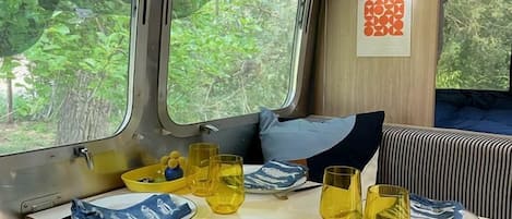 Un comedor con una mesa lista para dos personas, un banco y una ventana con vistas a la vegetación.