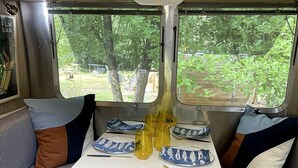 Ein kompaktes Wohnmobil-Interieur mit Esstisch, zwei gepolsterten Sitzbereichen und einem Fenster mit Blick auf Grünflächen.