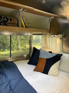 Una cama litera con ventana, una cama con almohadas y una cortina.