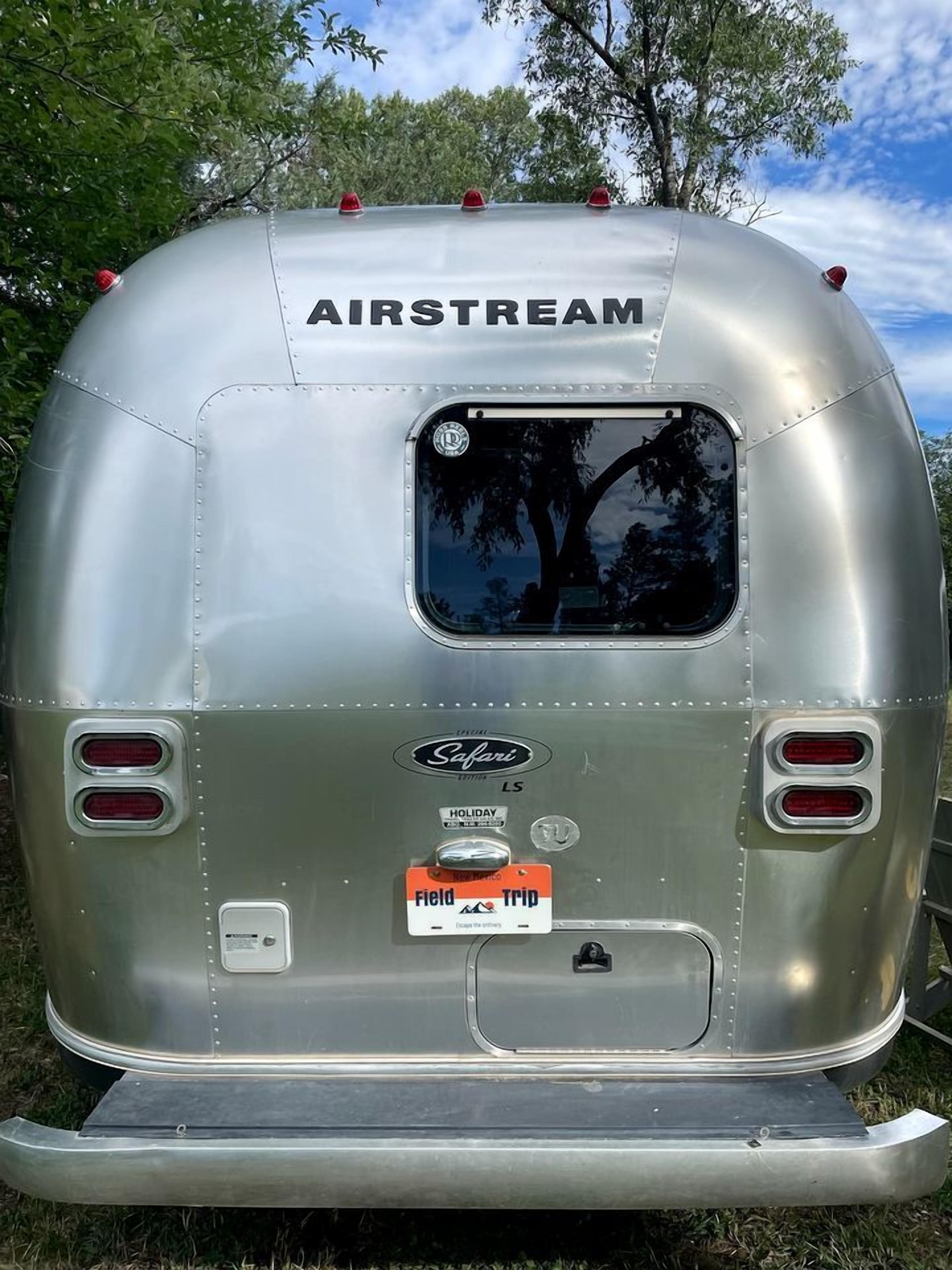 Une remorque argentée portant la marque « AIRSTREAM », avec une fenêtre et une plaque d’immatriculation indiquant « Field Trip ».