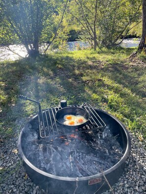Una parrilla portátil con huevos cocinándose, rodeada de grava y césped.