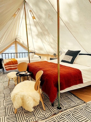 Ein Zelt mit Bett, Stuhl, kleinem Tisch und einem flauschigen weißen Sessel.
