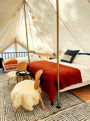 A tent with a bed, a chair, a small table, and a fluffy white chair.