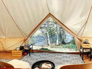 Una carpa con vistas a un bosque y al agua, una alfombra estampada y muebles de madera.