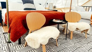 Ein Zimmer mit einem Bett, zwei Stühlen, einem kleinen Tisch und einem weißen, flauschigen Hocker.