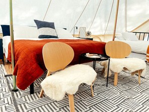 Ein Zimmer mit einem Bett, zwei Stühlen, einem kleinen Tisch und einem weißen, flauschigen Hocker.