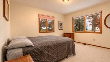A bedroom with a bed, two windows, a dresser, and a ceiling light.