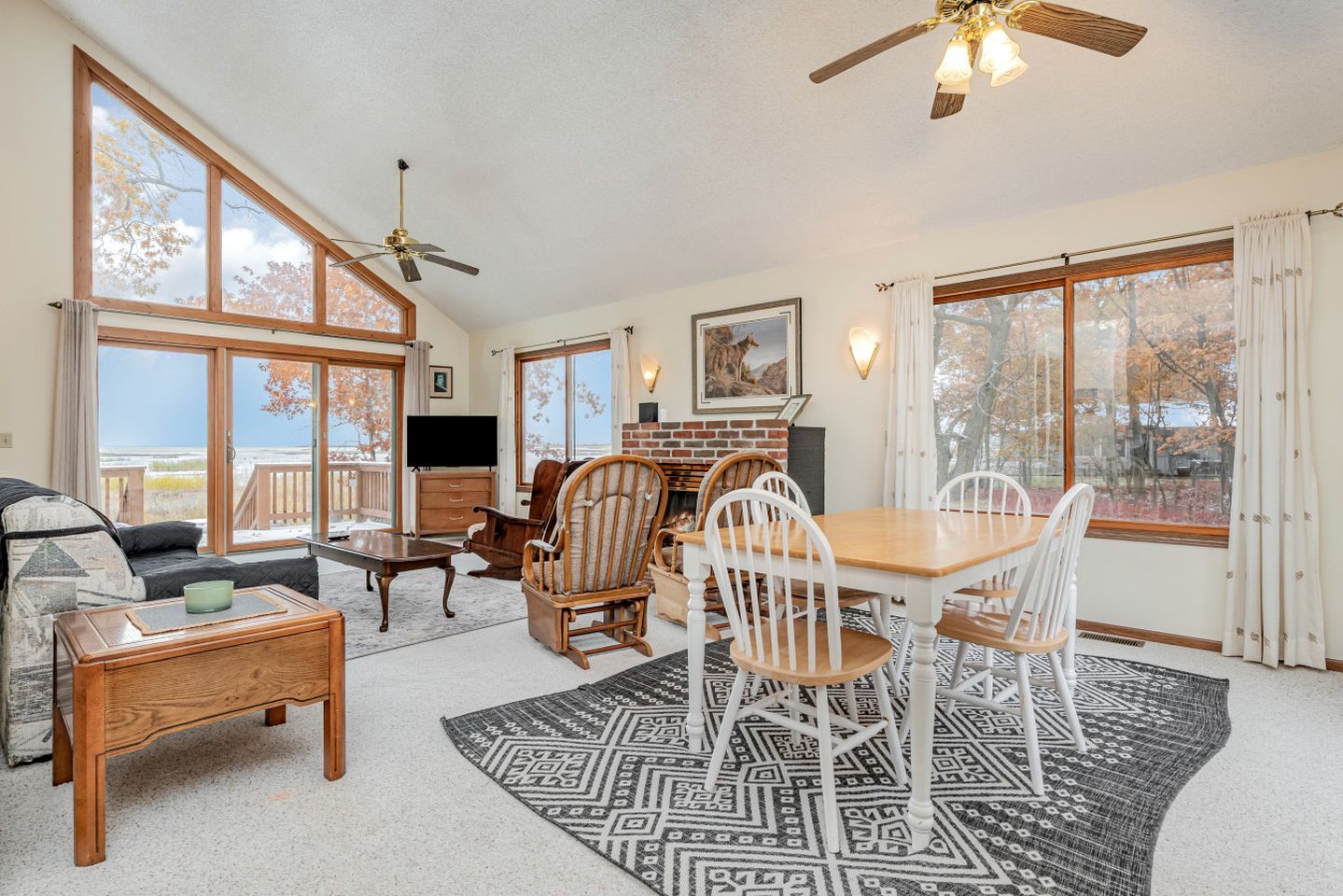 A spacious living room with a fireplace, a dining area, and large windows offering a view of the outdoors.