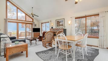 A spacious living room with a fireplace, a dining area, and large windows offering a view of the outdoors.