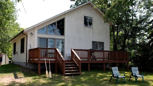 A single-story house with a deck, two chairs, and a lawn. - Comfy Sweet Cottage with BBQ Surrounded by Nature in Michigan (Au Gres)