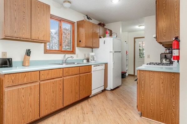 A kitchen with wooden cabinets, a white refrigerator, a sink, and a window.