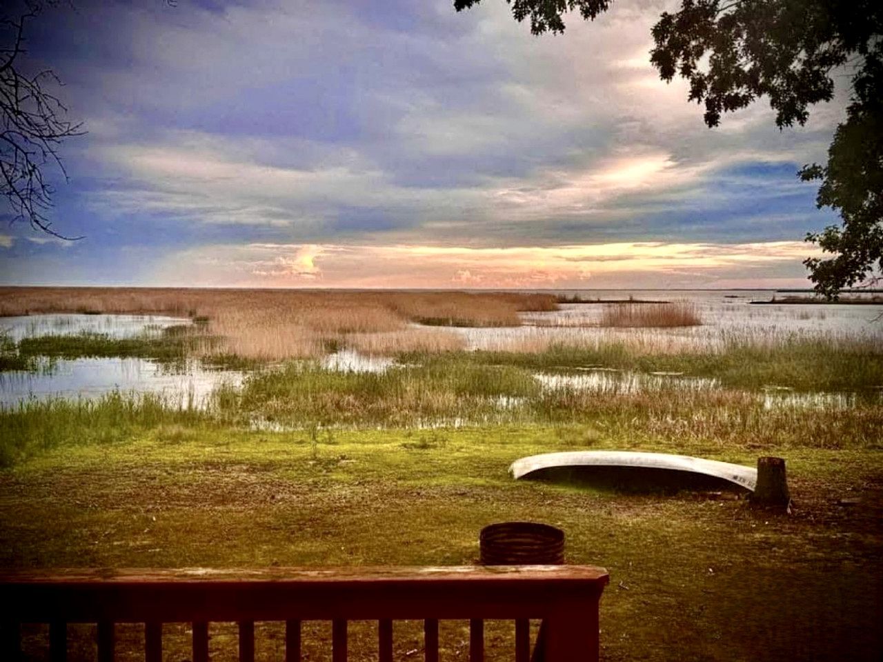A bench overlooking a marshy landscape with a sunset.