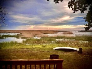 Un banc donnant sur un paysage marécageux, avec le soleil couchant à l’horizon.