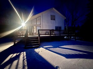 A snow-covered outdoor area with a wooden bench and a house in the background. - Comfy Sweet Cottage with BBQ Surrounded by Nature in Michigan (Au Gres)