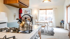 A kitchen with a stove, kettle, and wooden cabinets. - Comfy Sweet Cottage with BBQ Surrounded by Nature in Michigan (Au Gres)