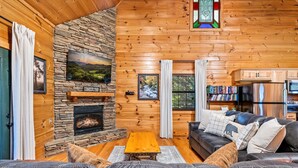 Un interior de cabaña acogedor, con chimenea de piedra, sofá de cuero y estantería llena de libros.