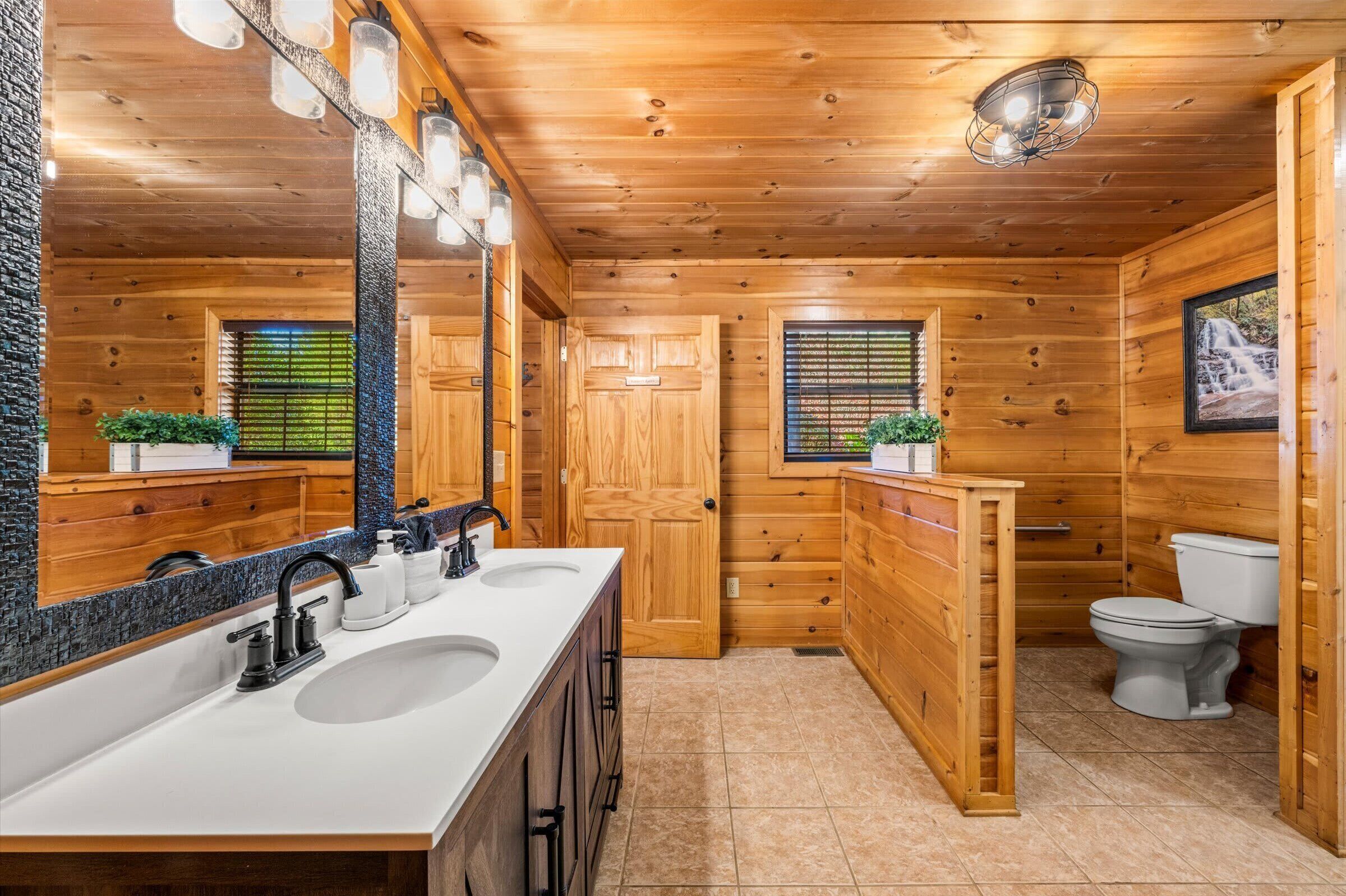 Un baño de cabaña de madera con un espejo grande, dos lavamanos y un inodoro.
