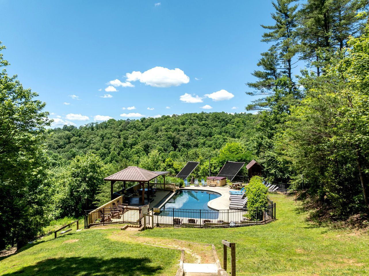 A pool with a deck, a gazebo, and a covered area with seating.