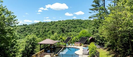 A pool with a deck, a gazebo, and a covered area with seating.