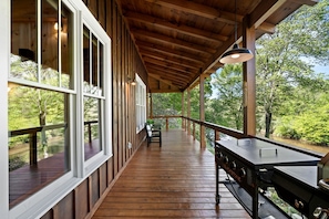 A covered wooden deck with large windows, a grill, and a view of the surrounding forest. - Incredible Riverfront Cabin Surrounded by Trees for an Unforgettable Escape in Nature in Blue Ridge, Georgia (Blue Ridge)