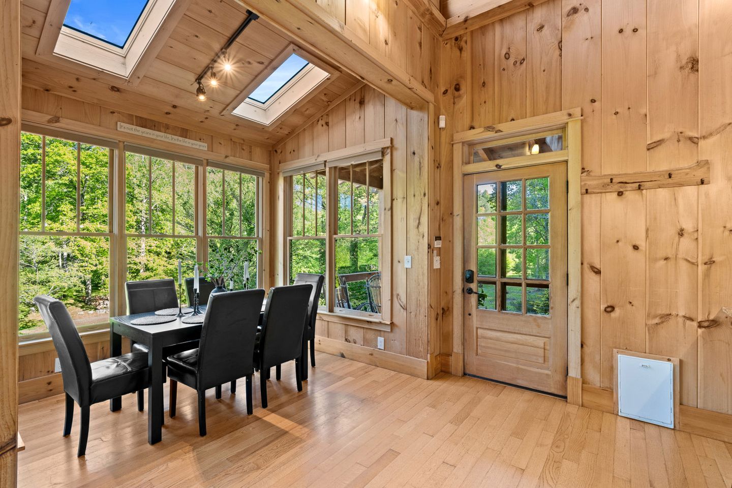 A wooden interior with a dining table, chairs, and large windows.