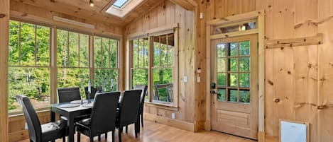 A wooden interior with a dining table, chairs, and large windows.