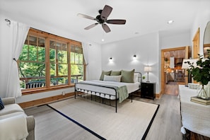 A bedroom with a bed, a ceiling fan, a window with curtains, a nightstand, and a view of the kitchen. - Incredible Riverfront Cabin Surrounded by Trees for an Unforgettable Escape in Nature in Blue Ridge, Georgia (Blue Ridge)