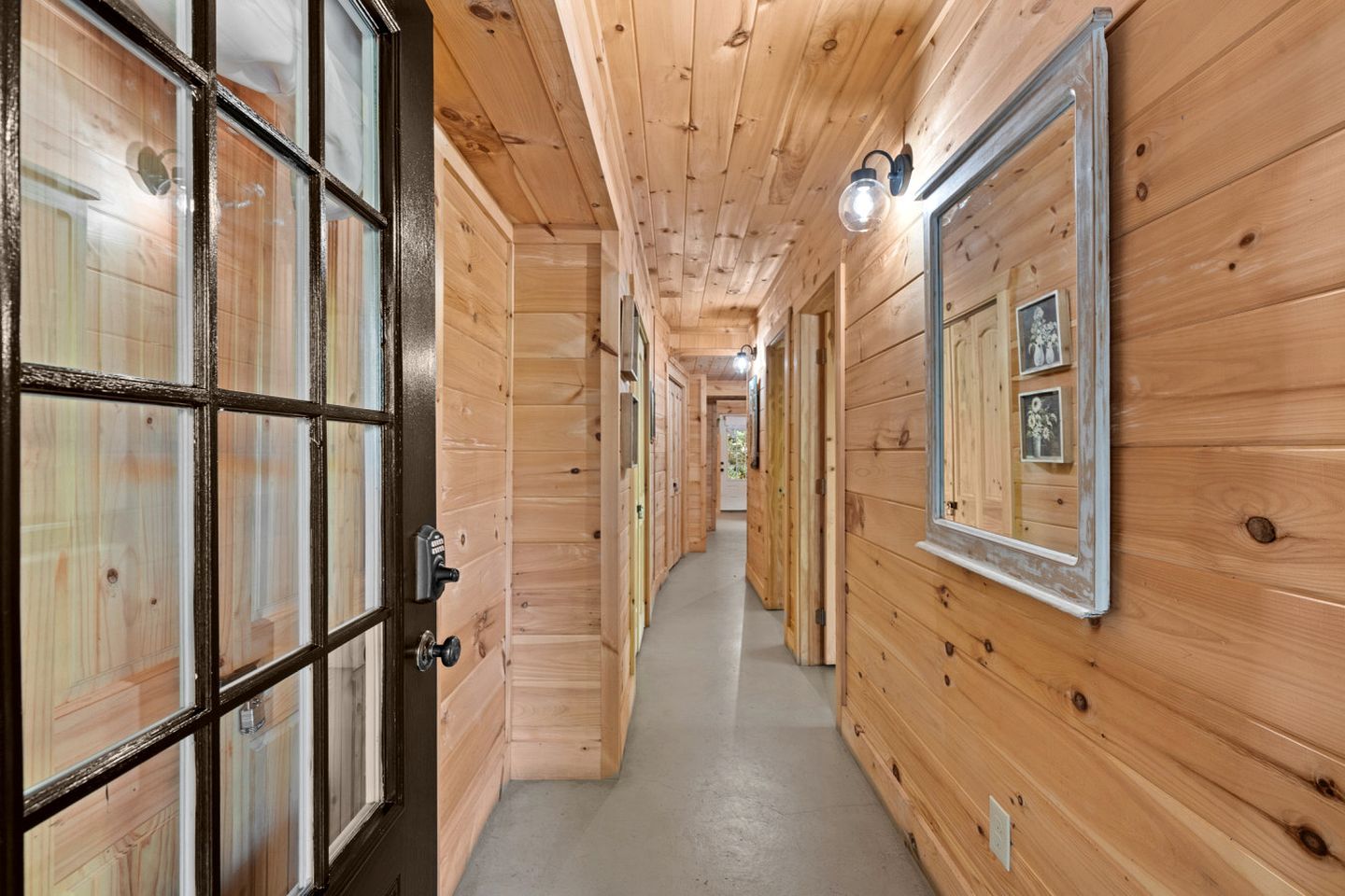 A wooden hallway with a door on the left and a wall with framed pictures on the right.