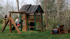 A wooden play structure with a swing set and climbing elements, surrounded by grass and trees. - Incredible Riverfront Cabin Surrounded by Trees for an Unforgettable Escape in Nature in Blue Ridge, Georgia (Blue Ridge)